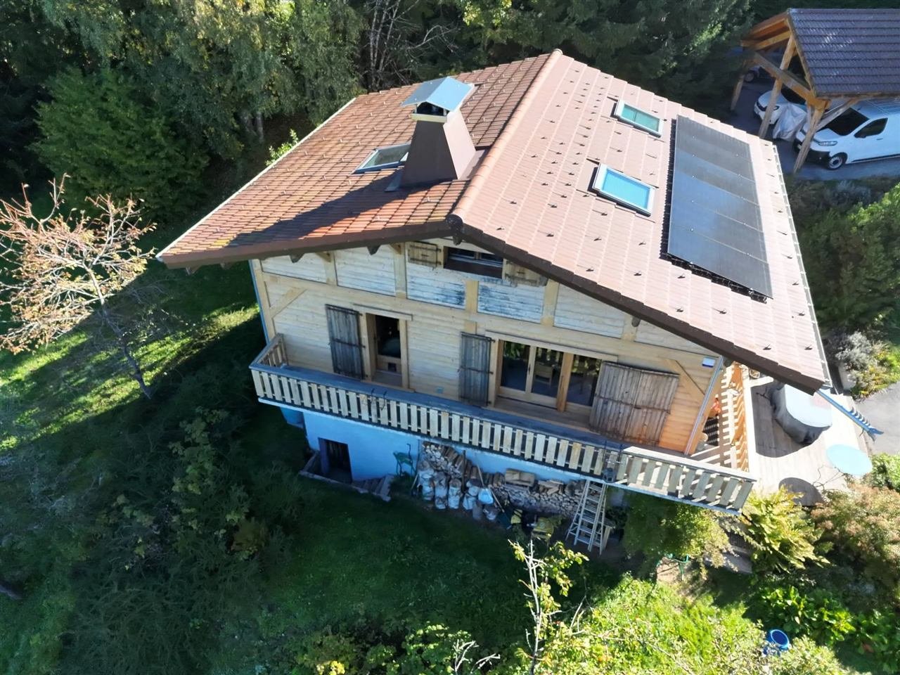 Chalet vu de dessus par drone : toiture en tuiles avec panneaux solaires, fenêtres de toit, cheminée et balcon